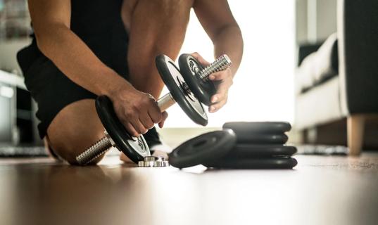 Person adding weights to a barbell while kneeling on the floor