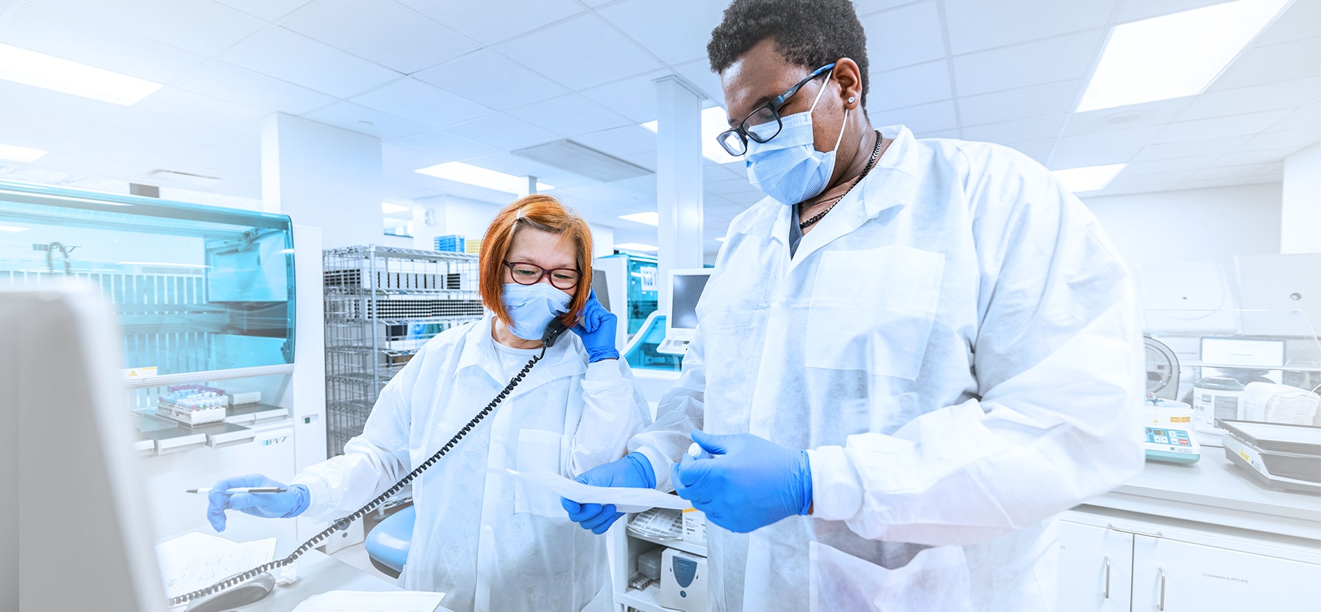 2 lab professionals, one on the phone and one holding a document and vial