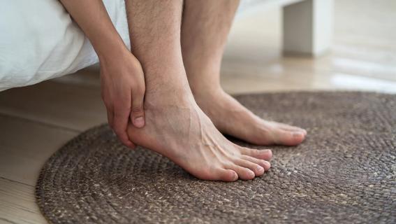 Hand rubbing their heel, sitting on edge of bed